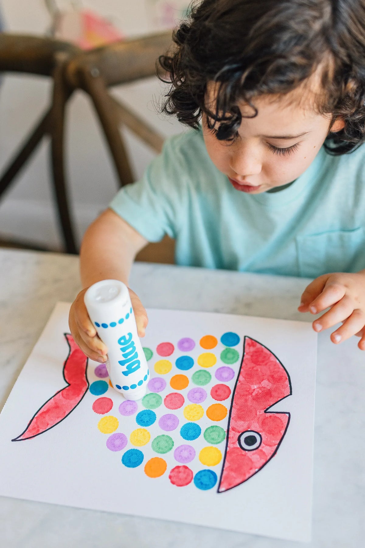 Child filling in a fish with dots using a blue Dot Marker