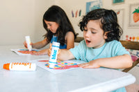Two kids making dot art at the table with Rainbow Dot Markers